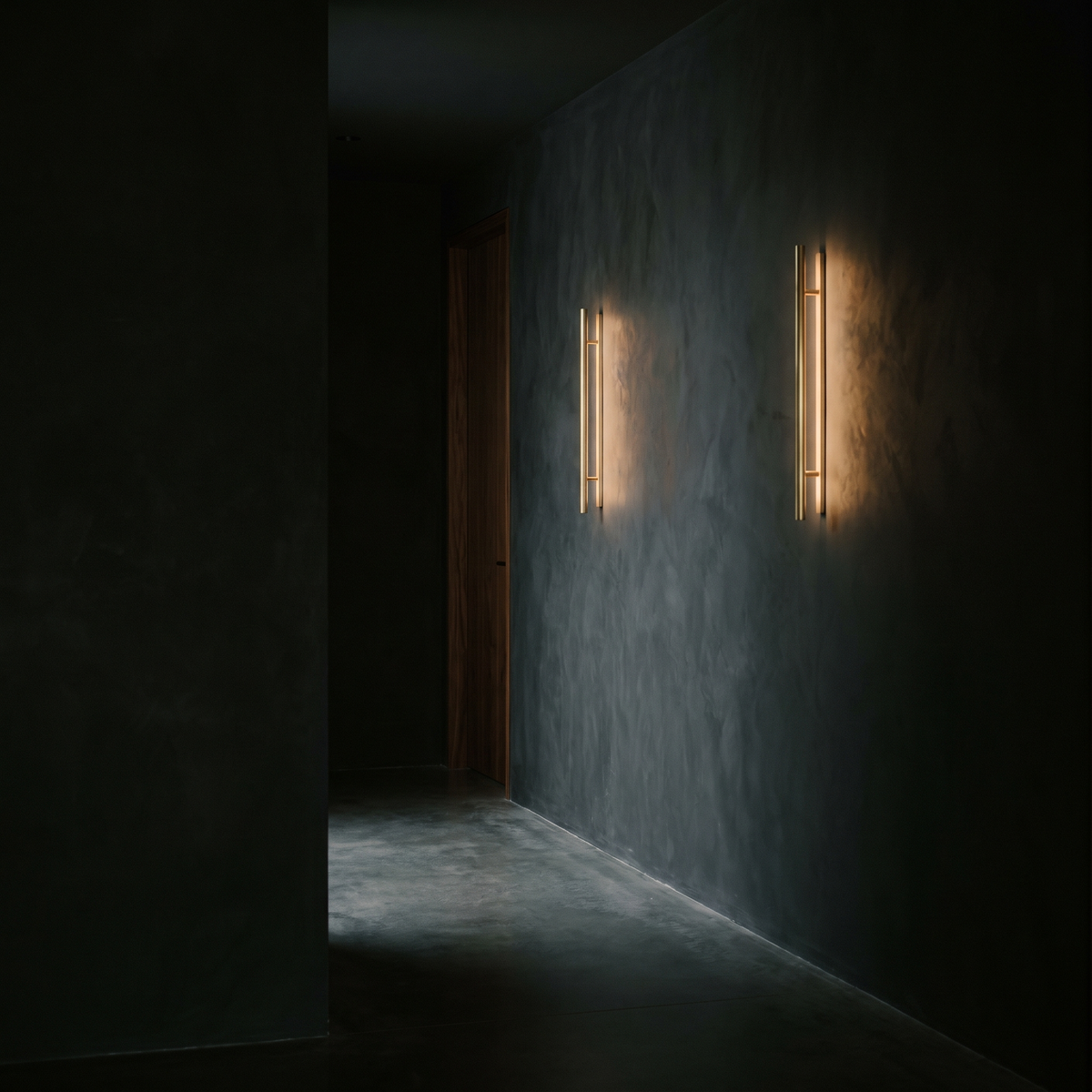 Two brass wall sconces lighting a dark plaster hallway wall