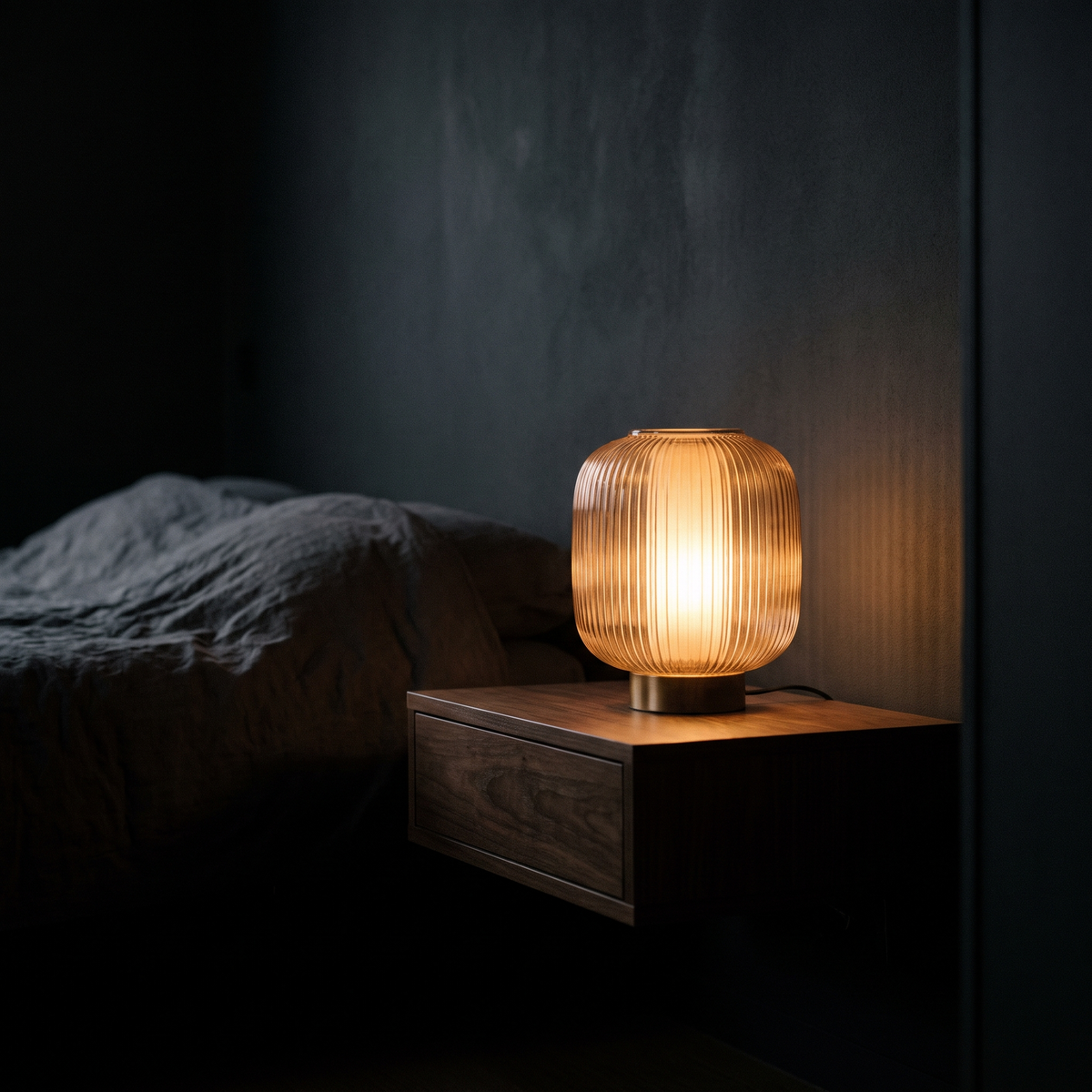 Ribbed glass table lamp glowing on a dark walnut bedside console