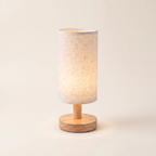 Linen Shade Wooden Bedside Lamp switched on, on a plain background