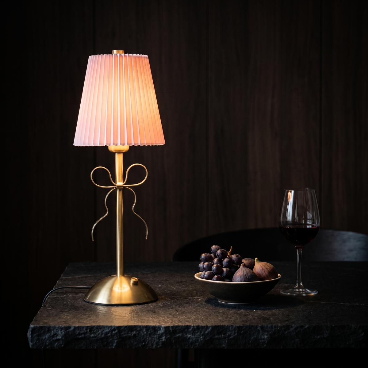 Pleated Bow Cordless Table Lamp on a black stone dining table with fruit and wine