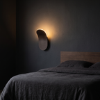 Wave-Form LED Wall Sconce mounted on a charcoal wall beside a bed in a dark bedroom