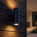 Cylinder Up & Down Outdoor Wall Light mounted on a dark timber-clad garden wall at night