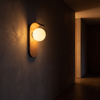 Oval Timber LED Wall Sconce mounted in a dark hallway washing the wall with warm light