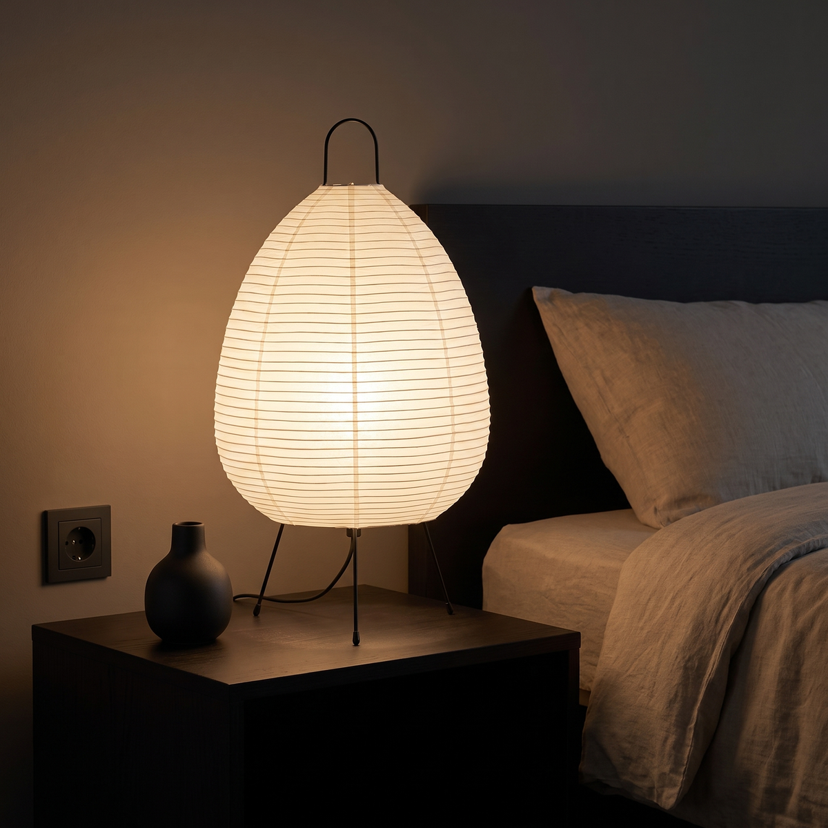Rice Paper Lantern Tripod Table Lamp shown to scale on a bedside table beside a small ceramic vase