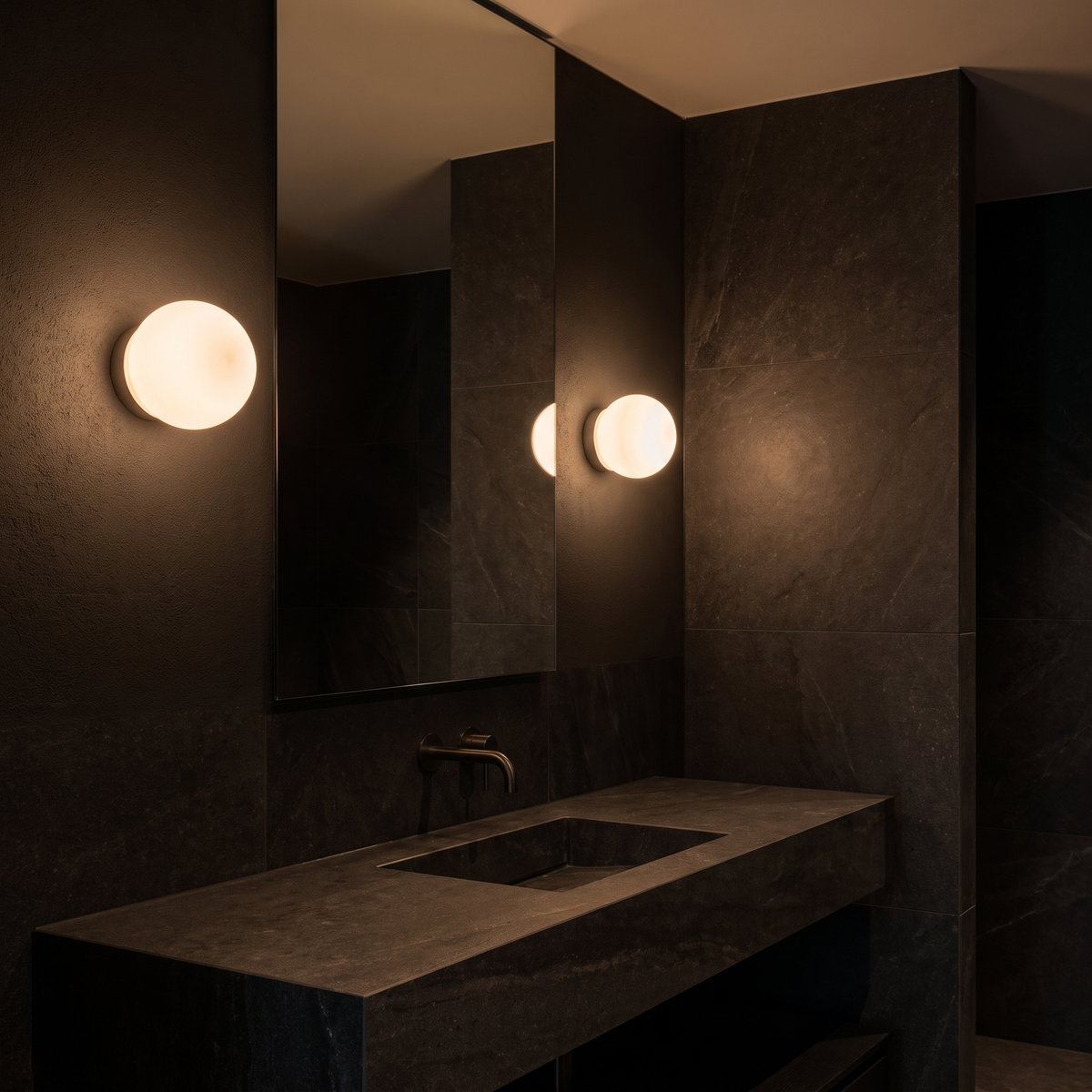 Floating milk glass globe wall sconce beside a bathroom mirror above a stone vanity