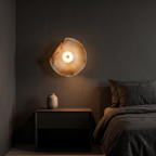 Wavy glass wall sconce shown to scale, mounted above a nightstand beside a bed