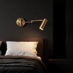 Brass swing arm cylinder wall sconce beside a bed, arm swung out as a reading light