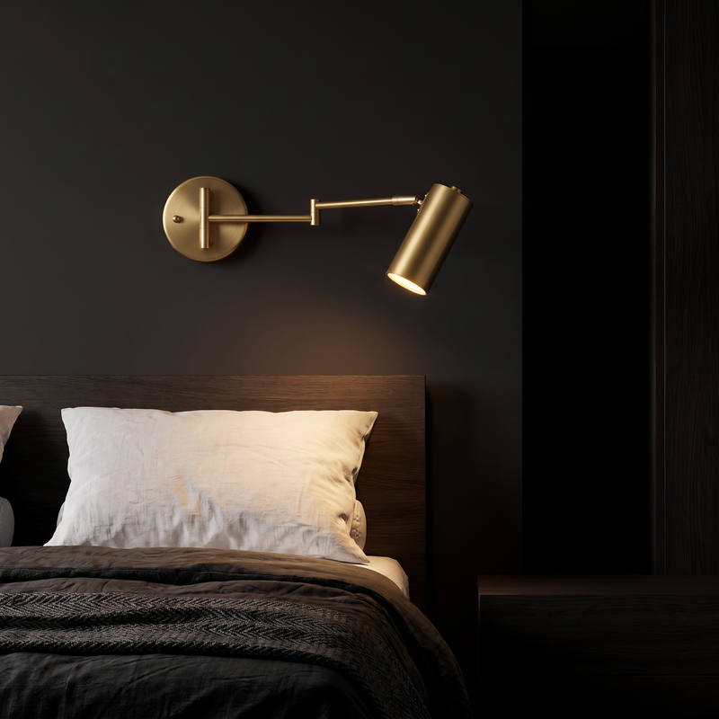 Brass swing arm cylinder wall sconce beside a bed, arm swung out as a reading light