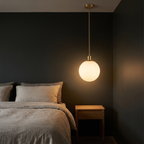 Milk glass globe pendant light hanging beside a bed above a small oak nightstand