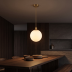Milk glass globe pendant light hanging low over a dark walnut dining table set with ceramic bowls