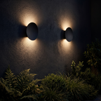 Two Black Pebble Wall Lights on a garden courtyard wall at night