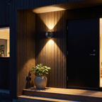 Modern Sphere Up Down Wall Light beside a black front door on a timber-clad porch at night