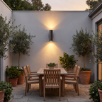 Modern Cylinder Up Down Outdoor Light on a courtyard wall above a patio dining table at dusk
