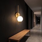 Modern Brass Globe Wall Sconce in a dark hallway above an oak bench