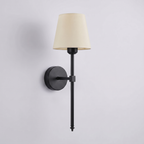 Cordless rechargeable wall sconce in matte black with a cream tapered fabric shade, on a plain grey studio background
