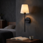 Matte black cordless wall sconce lit above a bedside table with no cable running down the wall