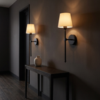 Two matte black cordless wall sconces lit above a console table in a dark hallway
