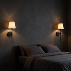 A pair of matte black cordless wall sconces mounted either side of a bed on a dark charcoal wall