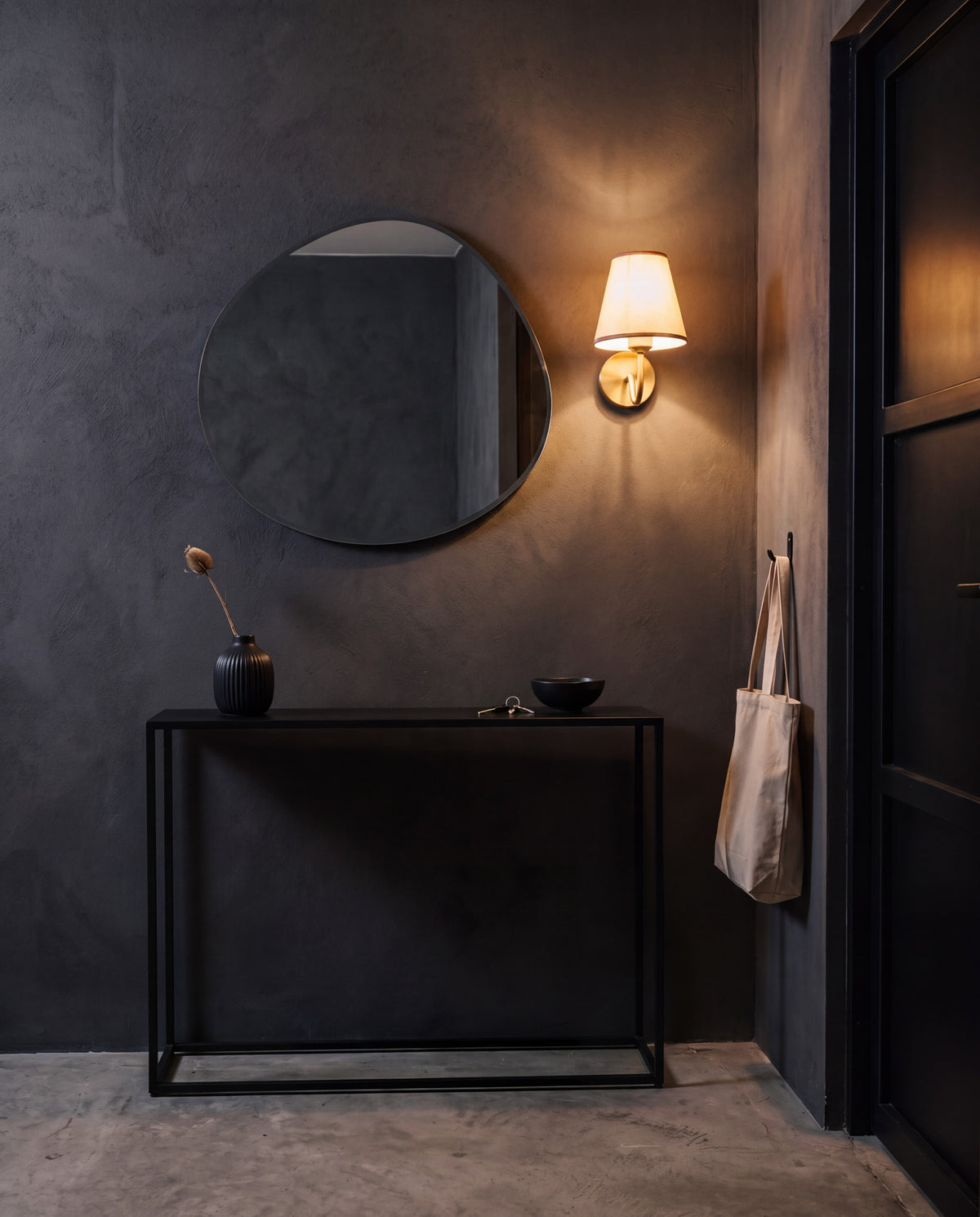Dark entryway with an organic mirror, black console and a brass wall sconce